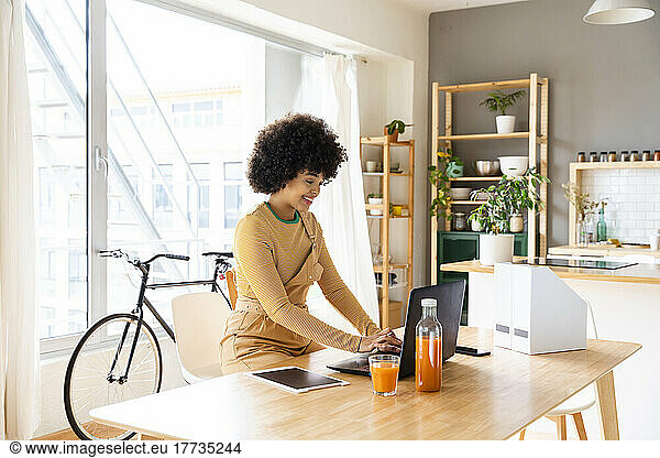 Happy woman using laptop sitting with tablet PC on table at home