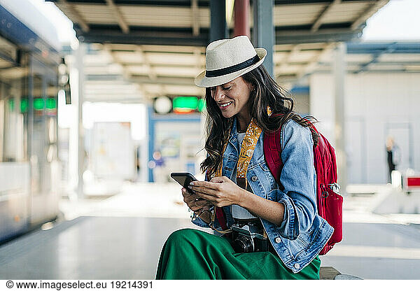 Happy woman using mobile phone at tram station