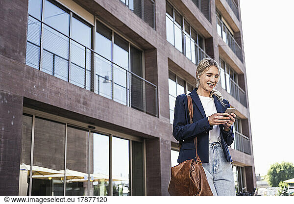 Happy woman using mobile phone in front of building