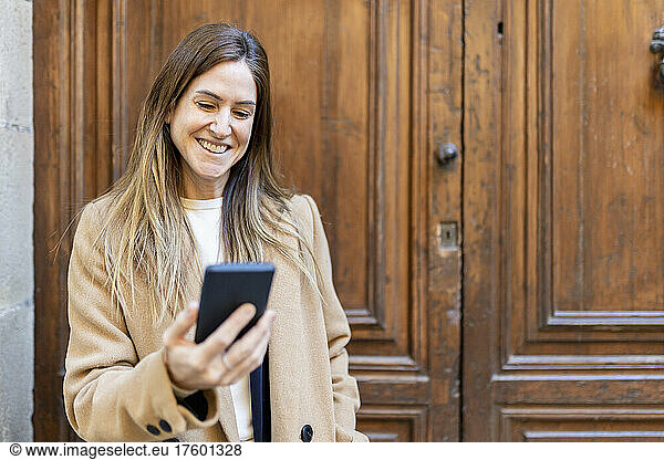 Happy woman using mobile phone in front of door