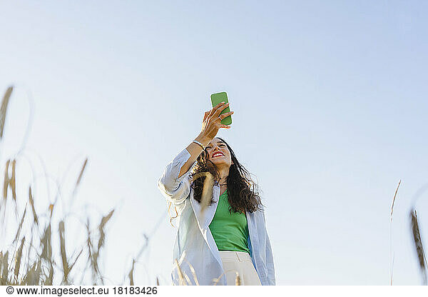 Happy woman using smart phone in field under clear sky