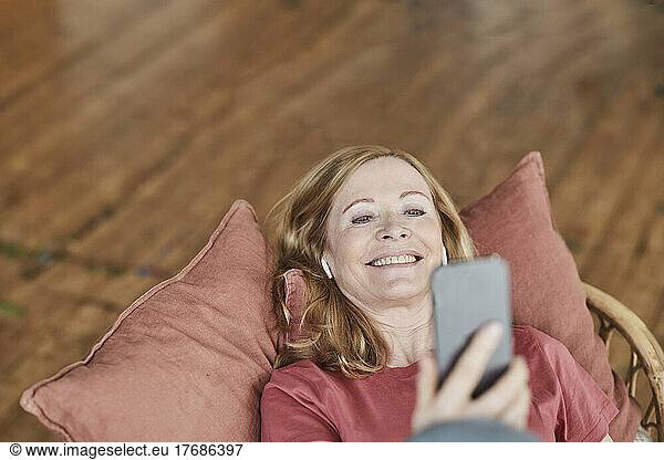 Happy woman using smart phone lying on sofa at home