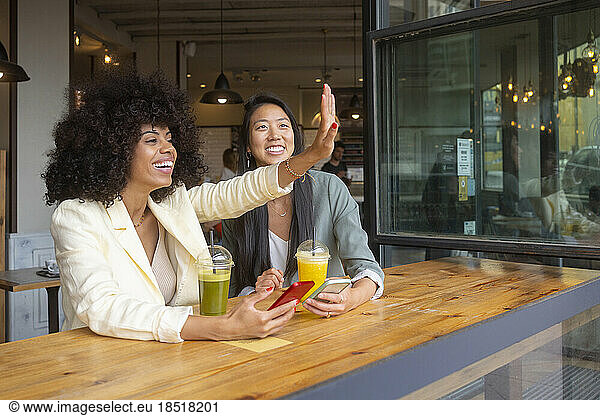Happy woman waving by friend sitting in cafe