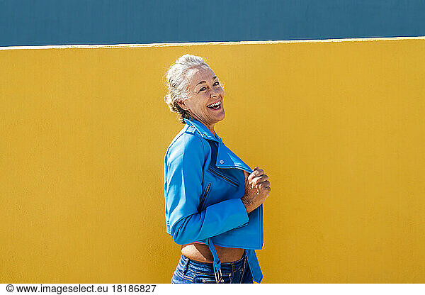 Happy woman wearing blue leather jacket by colored wall