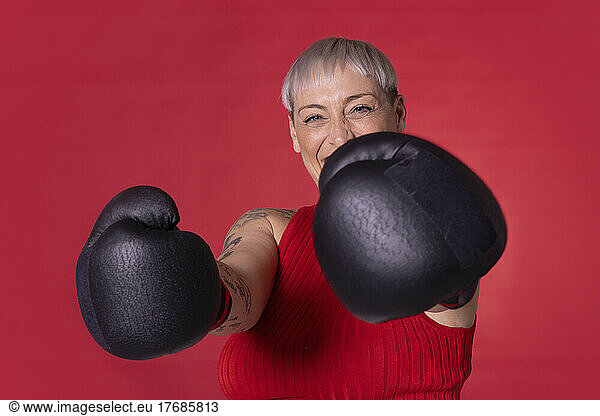 Happy woman wearing boxing gloves standing against red background