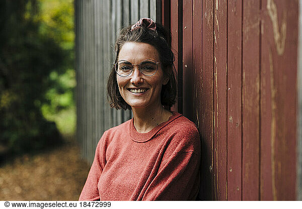 Happy woman wearing eyeglasses leaning on wooden wall