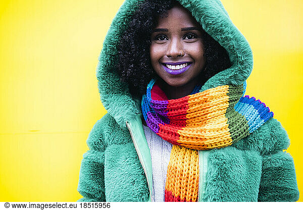 Happy woman wearing green hood jacket against yellow background