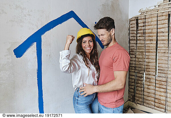 Happy woman wearing hardhat and flexing muscles by man at site