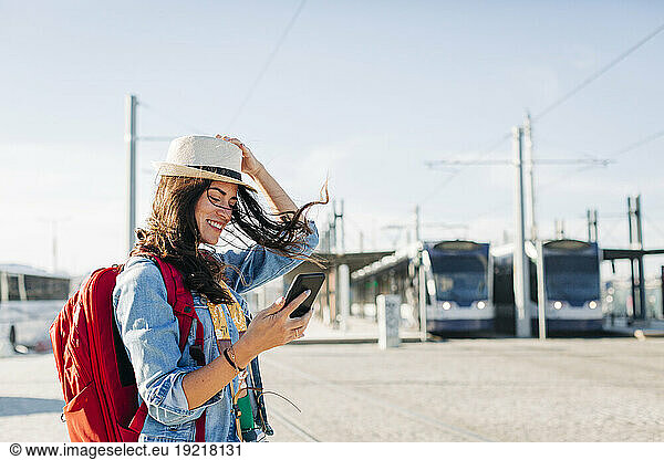 Happy woman wearing hat using smart phone on sunny day