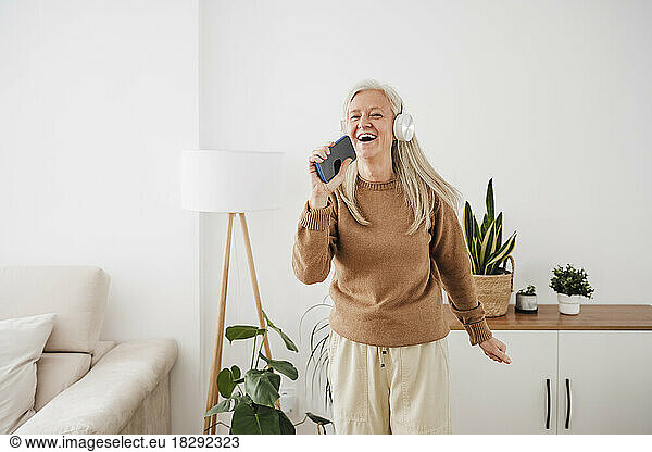 Happy woman wearing headphones dancing and singing at home