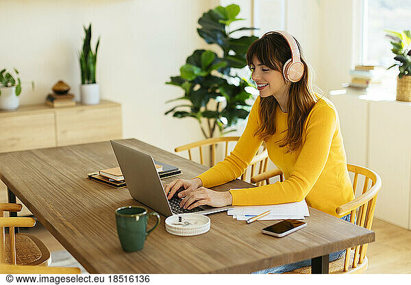 Happy woman wearing headphones working on laptop at home office