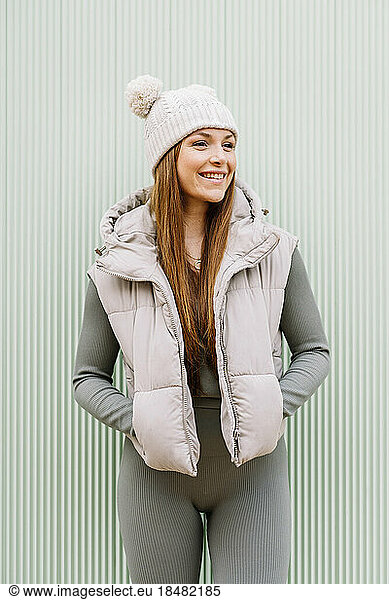 Happy woman wearing knit hat standing in front of green wall