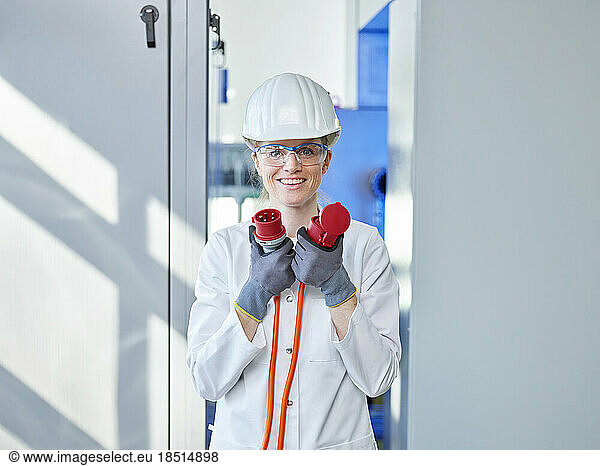 Happy woman wearing lab coat analyzing power plug in laboratory