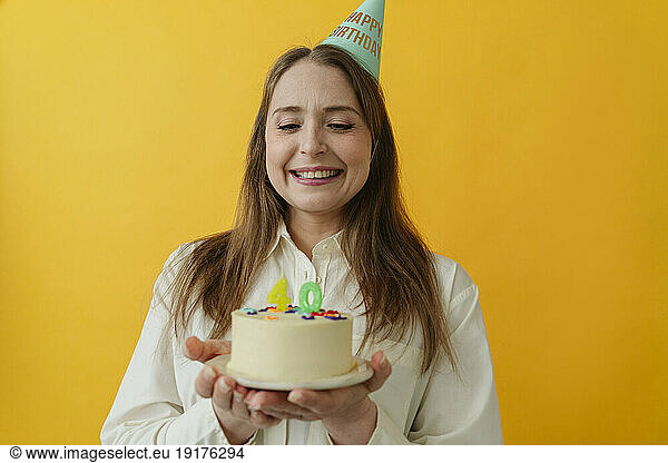 Happy woman wearing party hat holding birthday cake