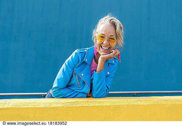 Happy woman wearing sunglasses in front of blue wall