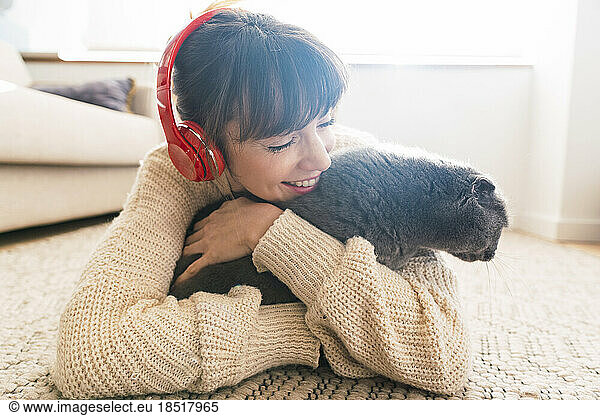 Happy woman wearing sweater embracing cat lying on carpet at home