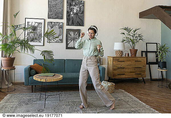 Happy woman wearing wireless headphones dancing in living room at home