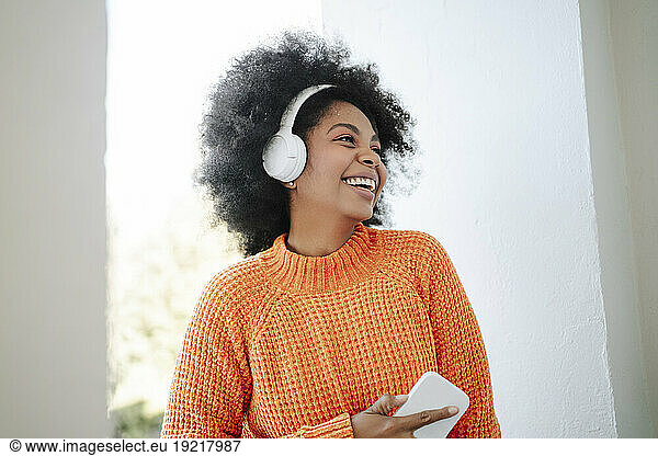 Happy woman wearing wireless headphones listening to music in balcony