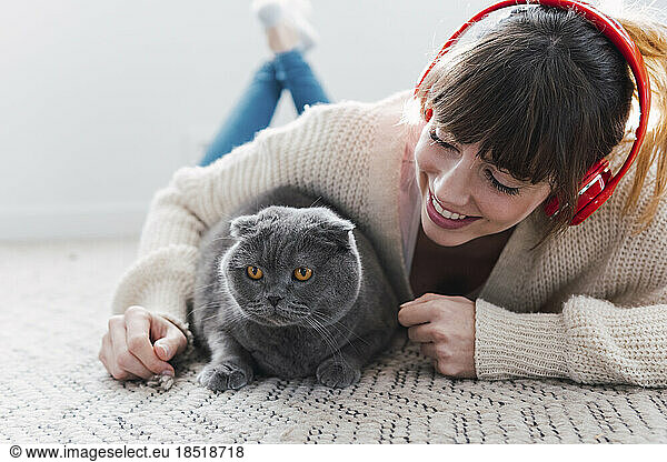 Happy woman wearing wireless headphones playing with cat at home