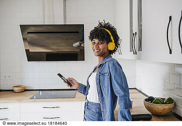Happy woman wearing wireless headphones standing with smart phone at home