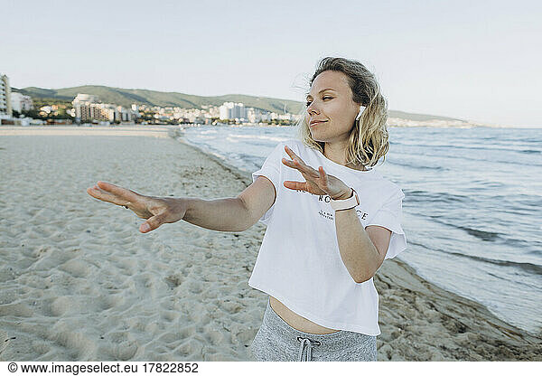 Happy woman wearing wireless in-ear headphones dancing on beach