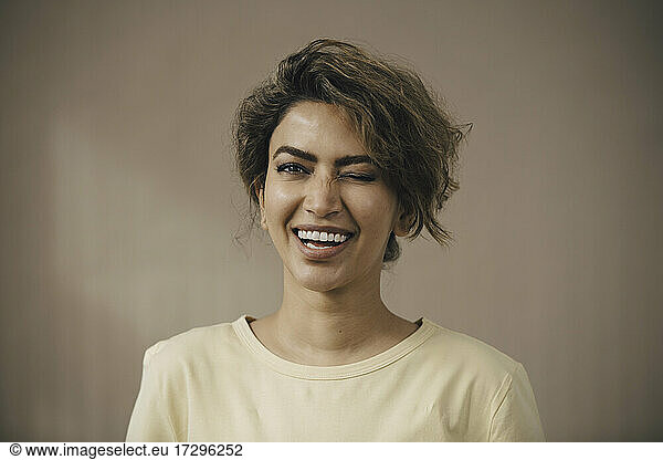 Happy woman winking eye against beige background