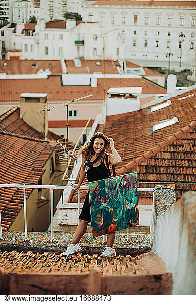 Happy woman with abstract art canvas standing on roof with view