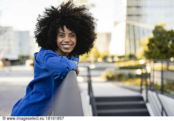 Happy woman with Afro hairstyle leaning on railing