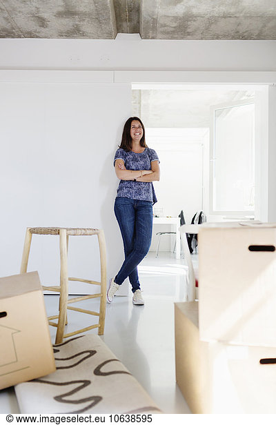 Happy woman with arms crossed leaning on wall in new home