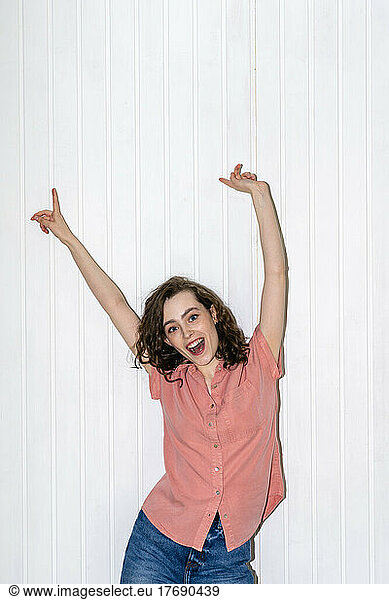 Happy woman with arms raised dancing in front of white wall