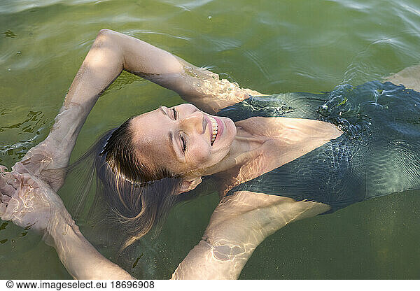 Happy woman with arms raised enjoying in lake