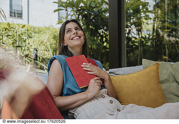 Happy woman with book sitting on sofa in back yard