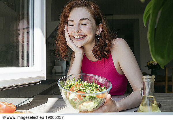 Happy woman with bowl of salad leaning on kitchen counter