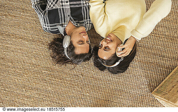 Happy woman with boyfriend wearing headphones lying on carpet at home