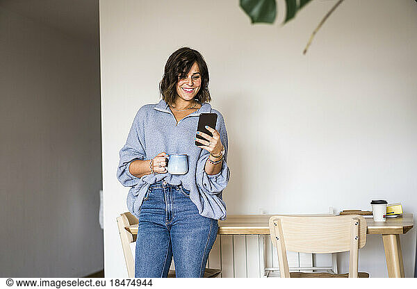 Happy woman with coffee cup using smart phone at home