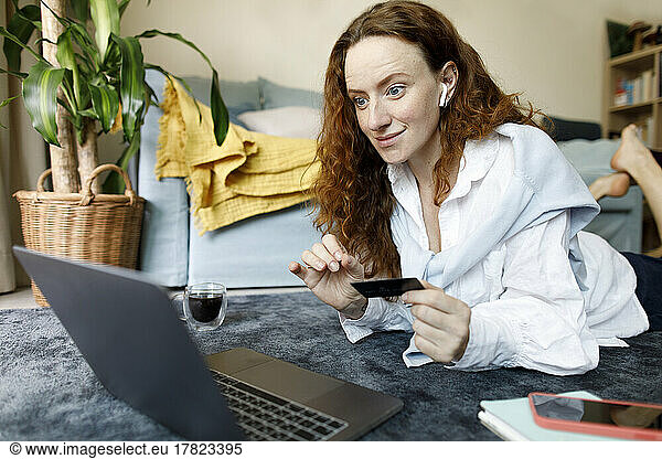 Happy woman with credit card making payment through laptop at home