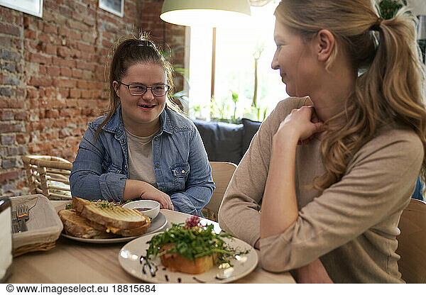 Happy woman with down syndrome having breakfast with friend in cafe