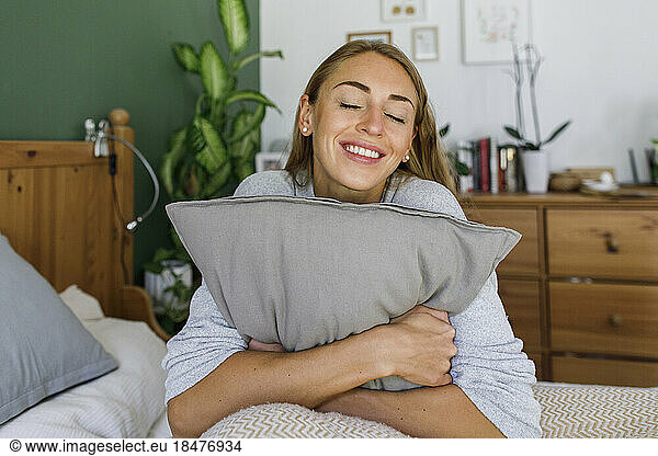 Happy woman with eyes closed hugging pillow in bed at home