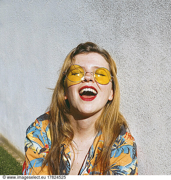 Happy woman with eyes closed wearing yellow sunglasses enjoying sunny day