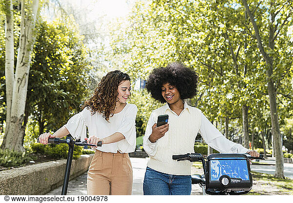 Happy woman with friend using smart phone in park