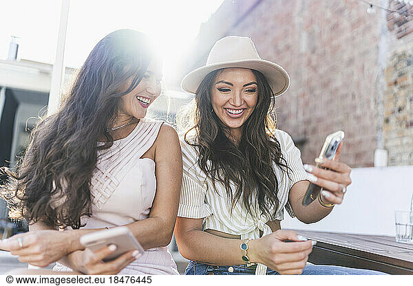 Happy woman with friend using smart phone on rooftop