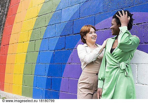 Happy woman with girlfriend in front of rainbow flag painted on wall