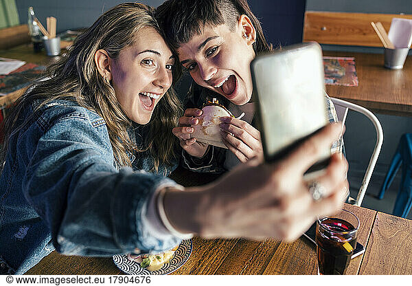 Happy woman with girlfriend taking selfie through smart phone