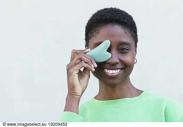 Happy woman with gua sha against white background