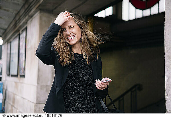 Happy woman with hand in hair holding smart phone