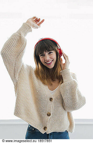 Happy woman with hand raised listening to music in front of wall