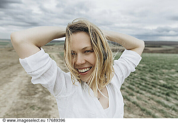 Happy woman with hands behind head in agricultural field