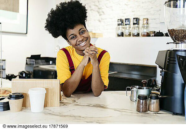 Happy woman with hands clasped leaning on checkout counter in cafe