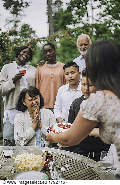 Happy woman with hands clasped looking at cake during birthday celebration