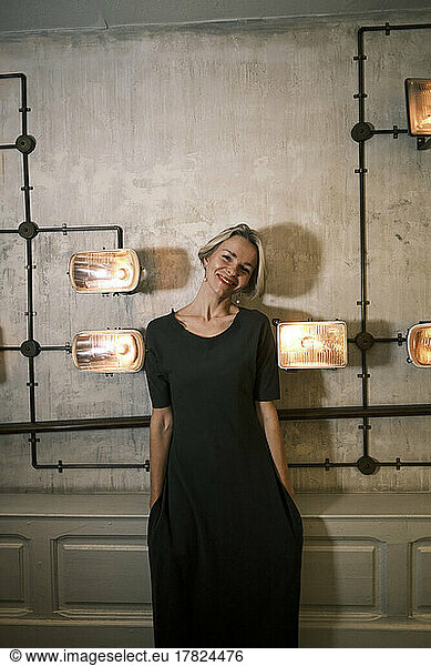 Happy woman with hands in pockets standing amidst illuminated lights